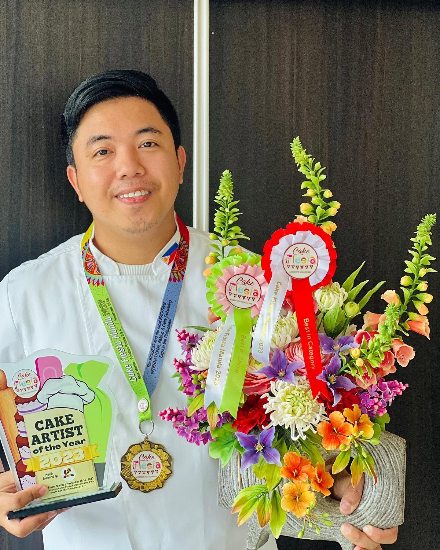 Jairuz Bon Bermudez Edaño holding his Cake Artist of the Year 2023 trophy and medal, with Best in Show and Best in Category ribbons